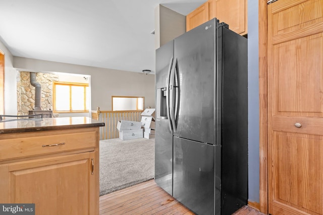 kitchen featuring refrigerator with ice dispenser, light brown cabinets, a wood stove, and light hardwood / wood-style flooring