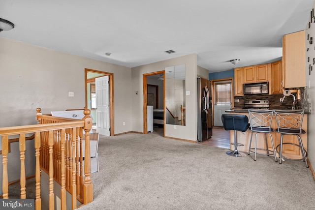 kitchen with tasteful backsplash, kitchen peninsula, light colored carpet, a kitchen bar, and appliances with stainless steel finishes