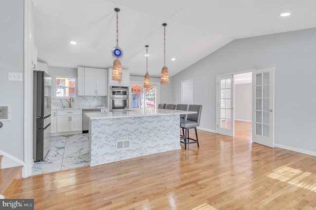 kitchen with a wealth of natural light, a center island, white cabinets, and appliances with stainless steel finishes