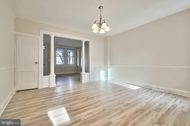 unfurnished room with an inviting chandelier, light hardwood / wood-style floors, and ornate columns