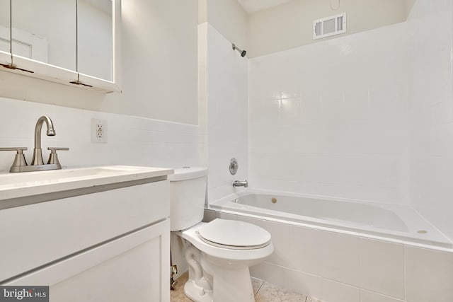 full bathroom featuring vanity, tile patterned floors, tiled shower / bath combo, toilet, and tile walls