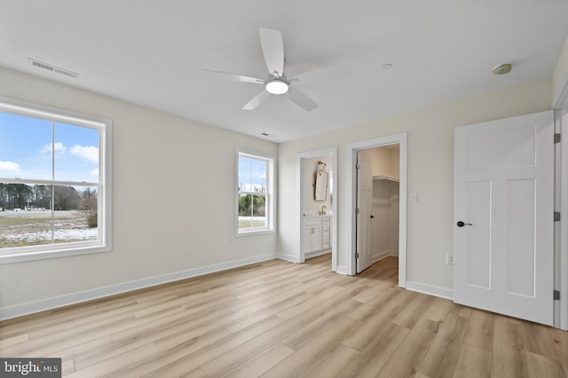 unfurnished bedroom featuring ensuite bathroom, light hardwood / wood-style flooring, a walk in closet, ceiling fan, and a closet