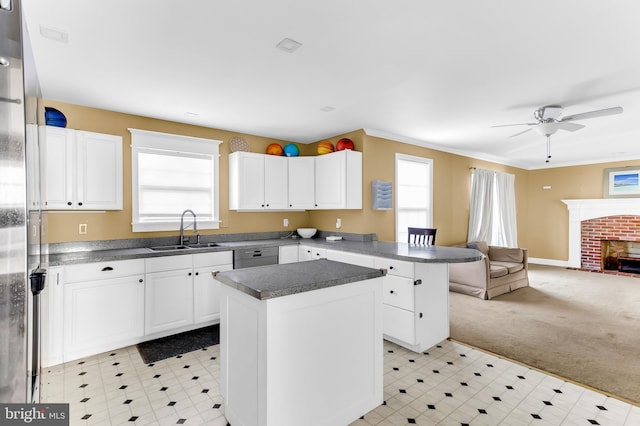 kitchen featuring a center island, a brick fireplace, white cabinetry, light carpet, and sink