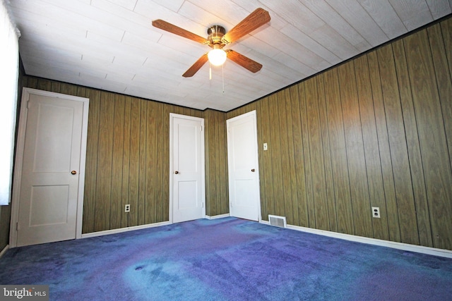 carpeted empty room with ceiling fan and wood walls