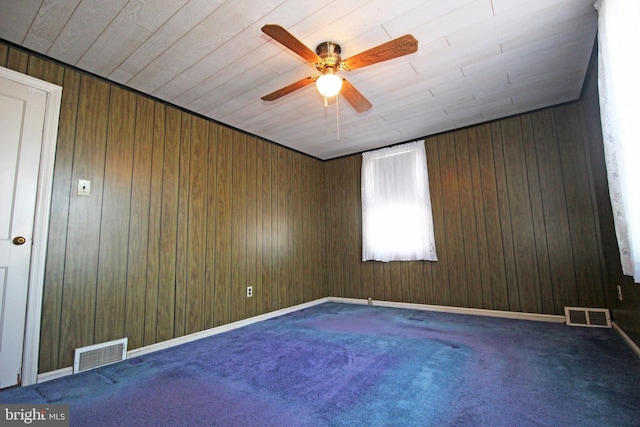 empty room with dark colored carpet, ceiling fan, and wood walls