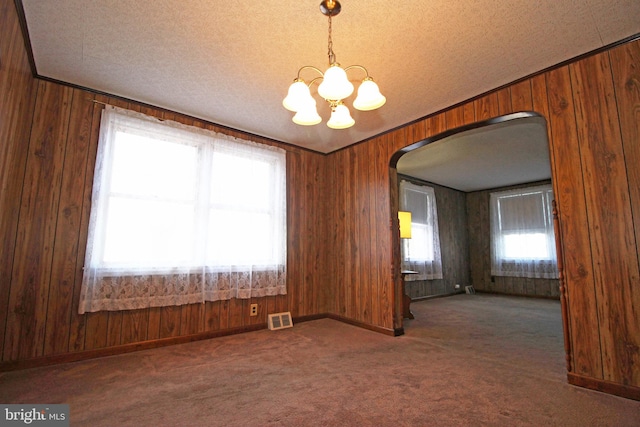 carpeted empty room with wood walls, a textured ceiling, and an inviting chandelier