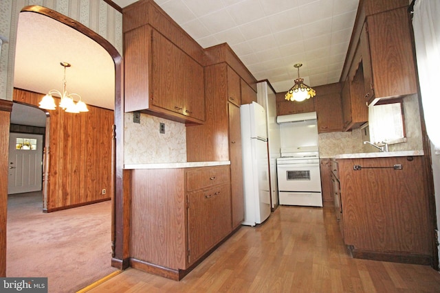 kitchen featuring wood walls, hanging light fixtures, white appliances, and light wood-type flooring