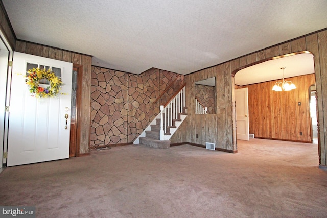 unfurnished living room featuring carpet flooring, a notable chandelier, wood walls, and a textured ceiling