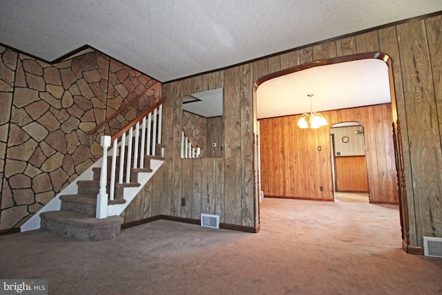 unfurnished living room with carpet flooring, a notable chandelier, wood walls, and a textured ceiling