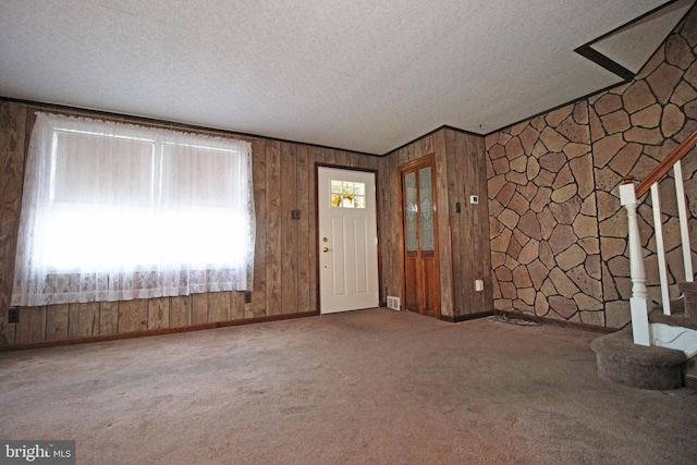 interior space featuring carpet, wood walls, and a textured ceiling