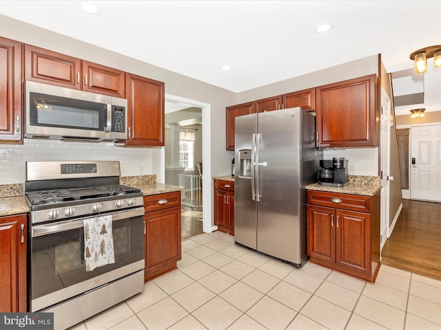 kitchen featuring tasteful backsplash, light stone countertops, stainless steel appliances, and light wood-type flooring