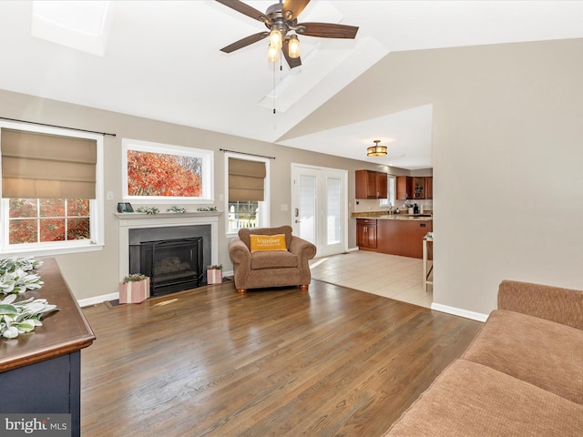 living room featuring hardwood / wood-style floors, ceiling fan, and lofted ceiling with skylight