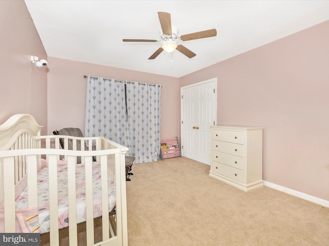 bedroom featuring ceiling fan, a closet, light colored carpet, and a nursery area