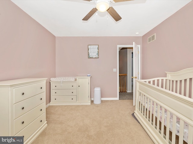 carpeted bedroom featuring ceiling fan and a crib