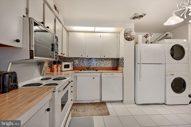 kitchen featuring pendant lighting, white appliances, white cabinets, sink, and stacked washing maching and dryer