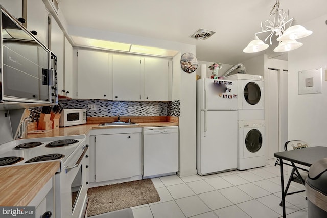 kitchen with pendant lighting, white appliances, white cabinetry, and stacked washer / dryer