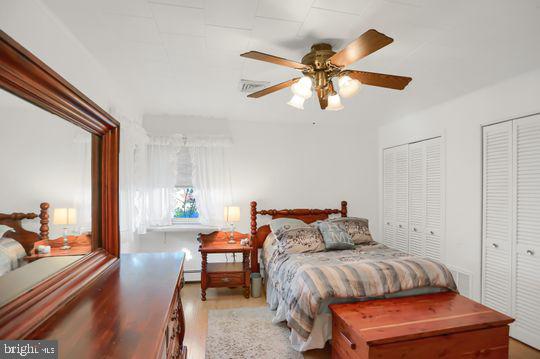 bedroom with light wood-type flooring, ceiling fan, and multiple closets