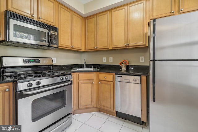 kitchen with appliances with stainless steel finishes, light tile patterned floors, dark stone counters, and sink