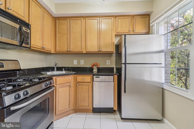 kitchen with appliances with stainless steel finishes, sink, dark stone countertops, and light tile patterned flooring