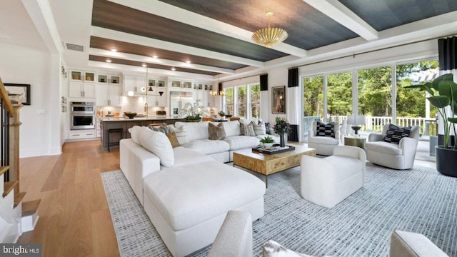 living room with an inviting chandelier, sink, beam ceiling, and light hardwood / wood-style floors