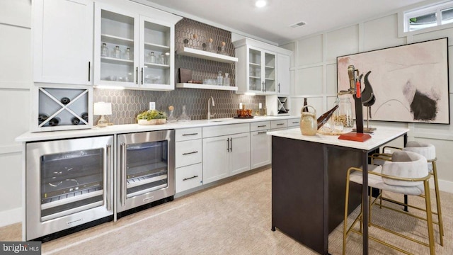 bar with white cabinets, decorative backsplash, light colored carpet, and beverage cooler