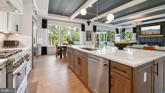 kitchen featuring sink, light stone countertops, appliances with stainless steel finishes, decorative light fixtures, and extractor fan