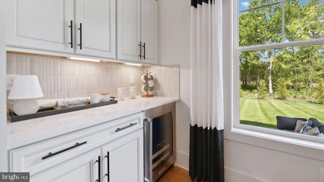 bar featuring wine cooler, backsplash, light stone countertops, and white cabinets