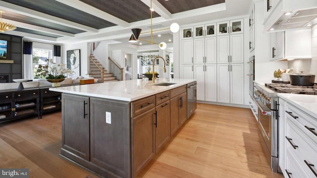 kitchen with stainless steel appliances, sink, a center island with sink, beamed ceiling, and white cabinets