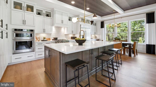 kitchen featuring white cabinetry, an island with sink, a breakfast bar area, hanging light fixtures, and stainless steel appliances