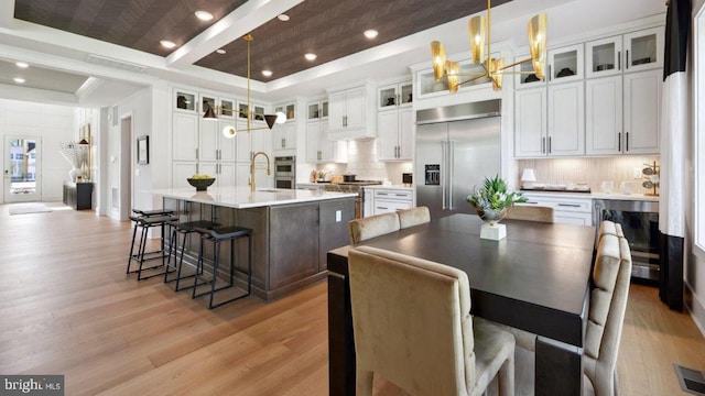 kitchen featuring stainless steel built in fridge, an island with sink, beverage cooler, and decorative light fixtures