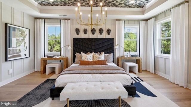 bedroom with a tray ceiling, light hardwood / wood-style flooring, and a notable chandelier