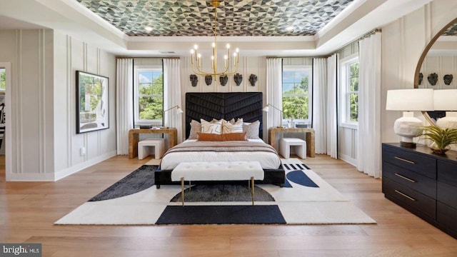 bedroom featuring light hardwood / wood-style floors, crown molding, a tray ceiling, and an inviting chandelier