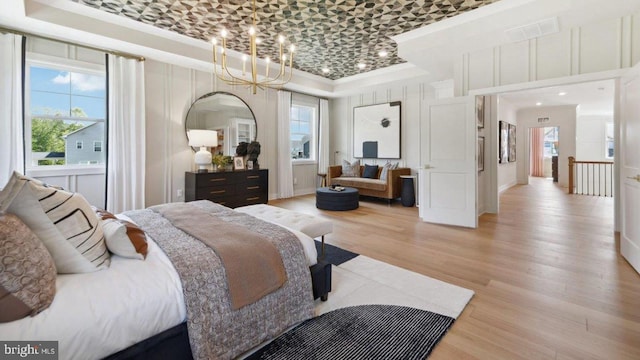 bedroom with a raised ceiling, ornamental molding, a chandelier, and light wood-type flooring