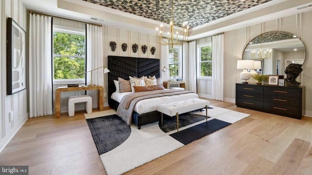 bedroom featuring multiple windows, light hardwood / wood-style floors, and a tray ceiling