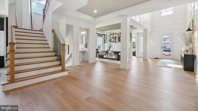 foyer featuring decorative columns, light hardwood / wood-style flooring, a towering ceiling, and a healthy amount of sunlight