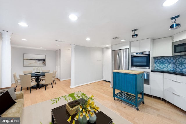 kitchen with light wood-type flooring, appliances with stainless steel finishes, tasteful backsplash, white cabinetry, and decorative columns