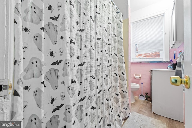 bathroom featuring toilet, wood-type flooring, tile walls, and walk in shower