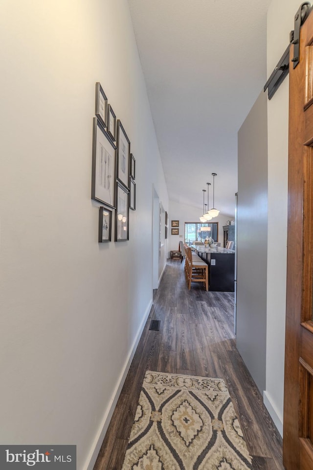 hallway with a barn door, dark hardwood / wood-style flooring, and lofted ceiling