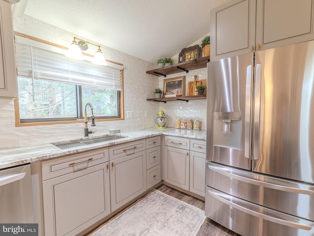 kitchen featuring a textured ceiling, sink, light stone countertops, and stainless steel appliances