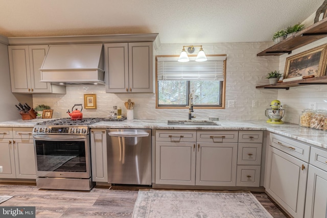 kitchen featuring appliances with stainless steel finishes, custom range hood, a textured ceiling, sink, and light hardwood / wood-style flooring