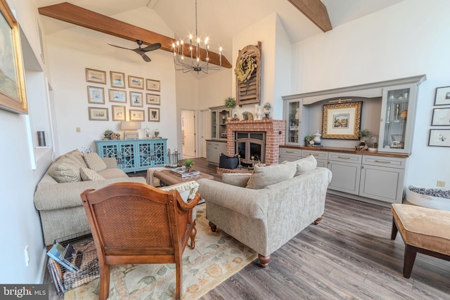 living room featuring ceiling fan with notable chandelier, wood-type flooring, high vaulted ceiling, beamed ceiling, and a fireplace