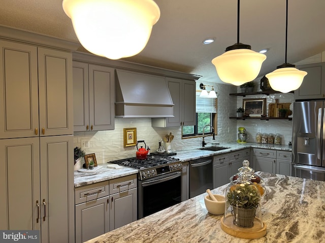 kitchen with sink, stainless steel appliances, light stone counters, premium range hood, and pendant lighting