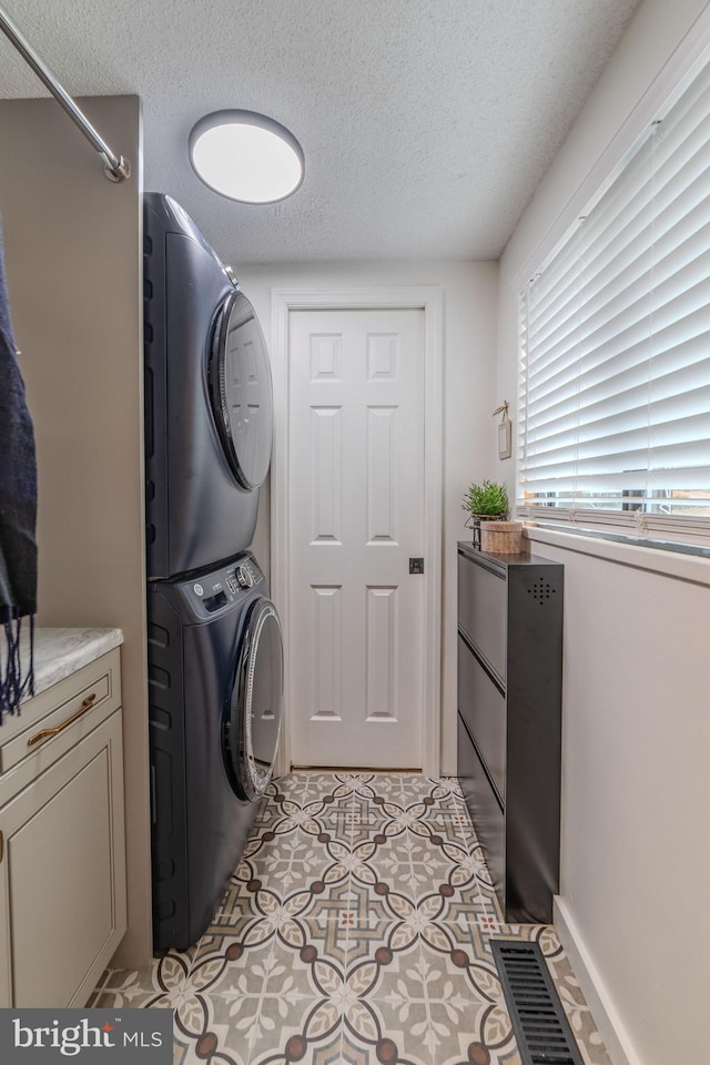 clothes washing area with a textured ceiling and stacked washer and clothes dryer