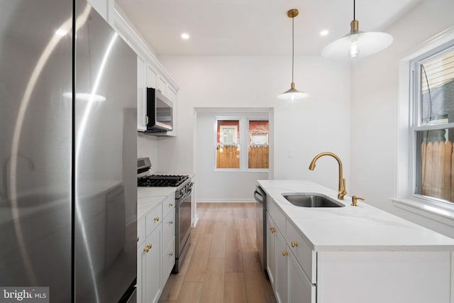 kitchen featuring appliances with stainless steel finishes, a kitchen island with sink, sink, decorative light fixtures, and white cabinetry