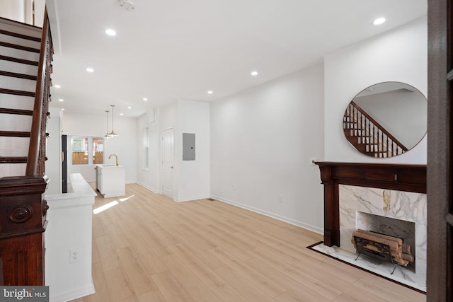 unfurnished living room with electric panel, a premium fireplace, sink, and light wood-type flooring