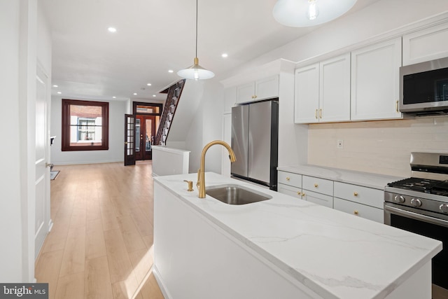 kitchen featuring appliances with stainless steel finishes, sink, light hardwood / wood-style floors, white cabinetry, and hanging light fixtures