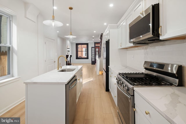 kitchen with pendant lighting, white cabinets, stainless steel appliances, and a kitchen island with sink