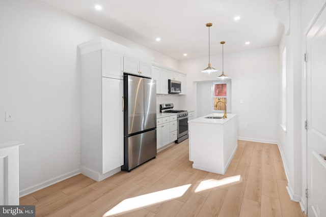 kitchen with pendant lighting, a center island with sink, white cabinetry, and appliances with stainless steel finishes