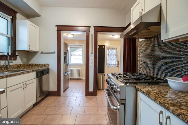 kitchen with stainless steel appliances, white cabinetry, radiator, and dark stone countertops