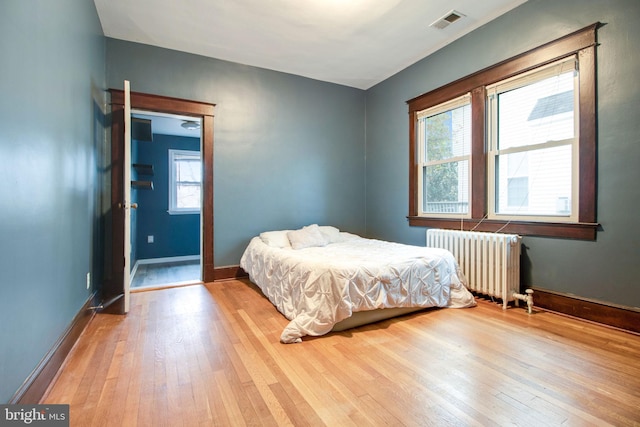 bedroom featuring radiator heating unit, light hardwood / wood-style flooring, and multiple windows